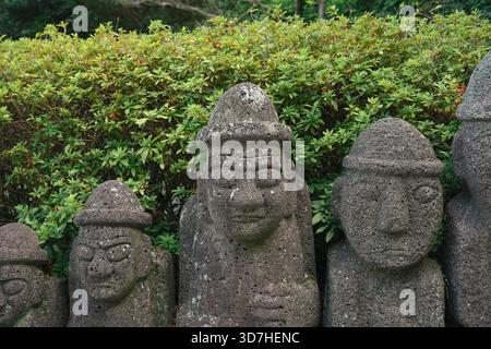 Dol Hareubang statues en pierre, le symbole de l'île de Jeju, Corée, debout côte à côte contre des buissons verts Banque D'Images