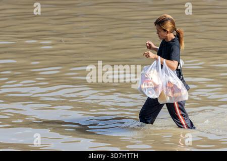 BANGKOK, THAÏLANDE, nov 09 2025, Une femme avec de nombreux sacs en plastique patère dans une rue inondée Banque D'Images