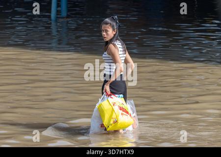 BANGKOK, THAÏLANDE, nov 09 2025, femme pataugant dans une rue inondée avec des sacs à provisions colorés Banque D'Images
