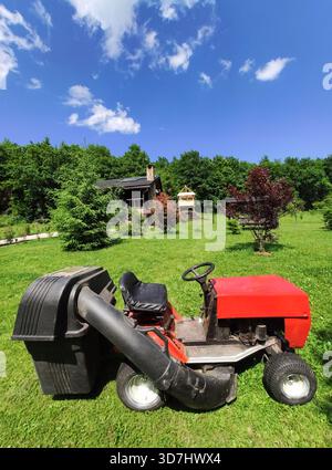un tracteur à gazon rouge, équipé d'un collecteur d'herbe, stationné dans une cour verte Banque D'Images