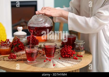 Jeune femme versant du thé viburnum chaud de la théière dans la tasse dans le salon Banque D'Images