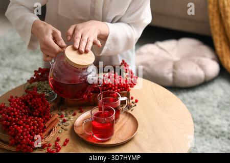 Jeune femme versant du thé viburnum chaud de la théière dans la tasse dans le salon Banque D'Images
