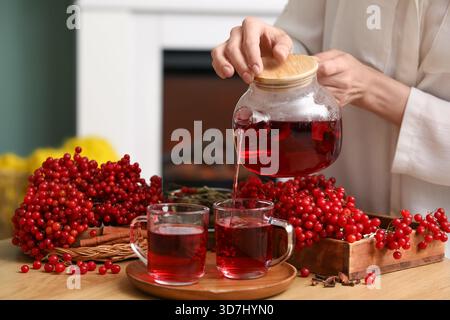 Jeune femme versant du thé viburnum chaud de la théière dans la tasse dans le salon Banque D'Images