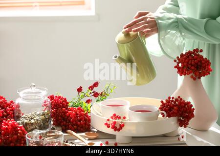 Jeune femme versant du thé viburnum de la théière dans la tasse à la maison Banque D'Images