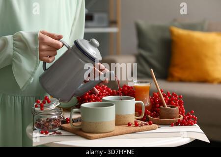 Jeune femme versant le thé viburnum savoureux de la théière dans la tasse à la maison Banque D'Images