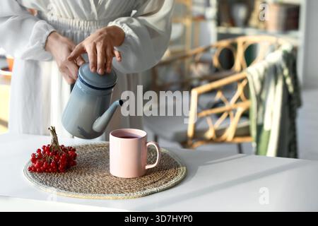 Jeune femme versant du thé viburnum de la théière dans la tasse à la maison Banque D'Images