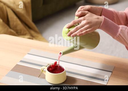 Jeune femme versant le thé viburnum savoureux de la théière dans la tasse à la maison, gros plan Banque D'Images