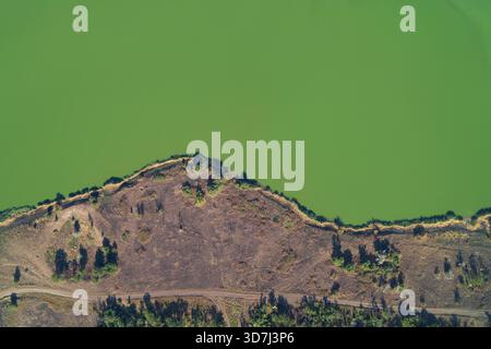 Prise de vue aérienne par drone montrant une frontière horizontale nette entre une prolifération d'algues vertes toxiques (pollution de l'eau) et un banc de terre brûlée. Risques environnementaux graves et effets du changement climatique. Banque D'Images