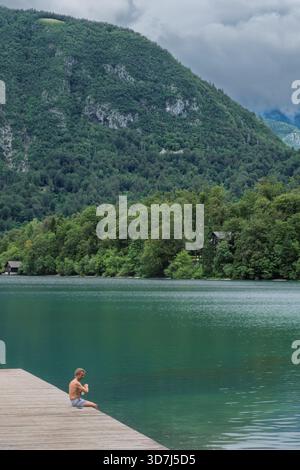 Personne assise sur la jetée en bois avec les pieds dans l'eau turquoise au lac Bohinj, Alpes juliennes, Slovénie. Banque D'Images