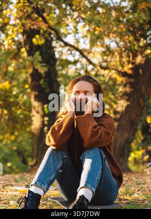 Jeune femme se relaxant dans le parc de la ville d'automne portant un pull confortable Banque D'Images