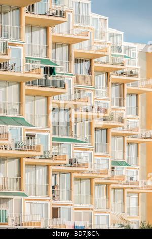 Balcons et fenêtres densément emballés d'un immeuble à plusieurs étages, formant un motif géométrique complexe avec des couleurs orange et blanc Banque D'Images