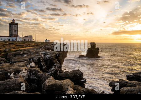 Peniche Portugal 9 novembre 2025. Un phare se dresse sur un promontoire rocheux face à une pile de mer au coucher du soleil. Banque D'Images
