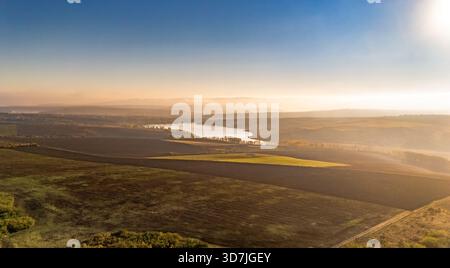 Vue drone du lac Dumbrava près de Iași, Roumanie, tôt le matin. L'eau calme, la brume et les couleurs d'automne créent un paysage paisible. Banque D'Images