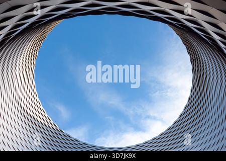 Vue rapprochée extrême regardant à travers la lucarne circulaire oculus et le treillis métallique texturé du bâtiment Messe Basel contre un ciel bleu Banque D'Images