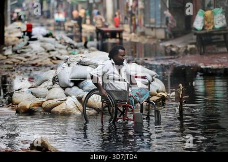 Un homme en fauteuil roulant se fraye un chemin à travers une eau noire profonde et profonde sur le Pipe Rasta de North Jurain à Dhaka. Les résidents disent que le drainage de la région Banque D'Images