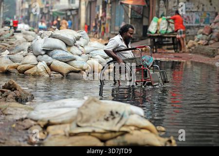 Un homme en fauteuil roulant se fraye un chemin à travers une eau noire profonde et profonde sur le Pipe Rasta de North Jurain à Dhaka. Les résidents disent que le drainage de la région Banque D'Images