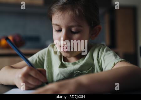 artiste jeune se concentrant, adolescent se concentre profondément sur les croquis détaillés dans un éclairage de cuisine calme Banque D'Images