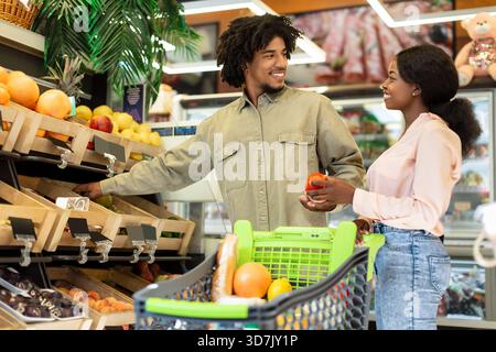 Couple aime faire du shopping ensemble dans une épicerie, en sélectionnant des fruits frais par un après-midi ensoleillé Banque D'Images