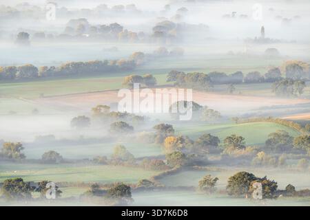 Le soleil tôt le matin se brise à travers la brume basse au-dessus des niveaux du Somerset, vu de Deer Leap sur les collines de Mendip, Angleterre, Royaume-Uni. Banque D'Images
