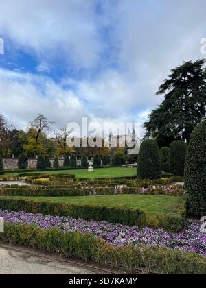 Le parc El Retiro à Madrid présente des jardins géométriques, des parterres de fleurs violettes et un ciel bleu et nuageux spectaculaire avec des bâtiments urbains au loin. Banque D'Images