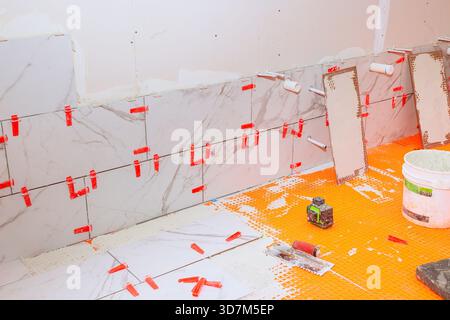 Les travailleurs sont occupés à installer de grandes tuiles de marbre sur le mur de la salle de bains en utilisant des entretoises pour des espaces uniformes. Banque D'Images