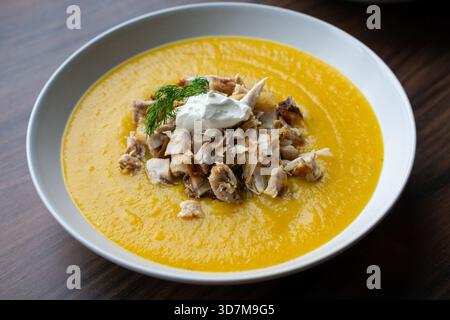 La photographie capture un gros plan détaillé de la soupe à la crème de citrouille garnie de poulet et d'une petite portion de crème. Banque D'Images