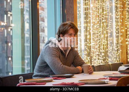 Réfléchi beau jeune homme attendant et buvant du café dans un café et regardant loin. Banque D'Images