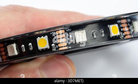 Macro détail de bande de LED RGBW en gros plan avec pastilles de soudure 5 V et marque de ligne de coupe, ruban lumineux CMS flexible tenu à la main, canaux RGB adressables plus blanc o Banque D'Images