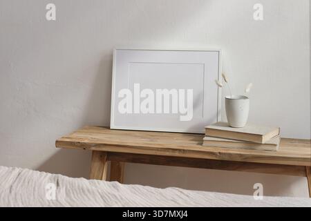 Maquette d'affiche de cadre photo blanc horizontal. Table en bois vintage, banc avec tasse en céramique, queue de lapin herbe sèche, vieux livres. Fond de mur blanc Banque D'Images
