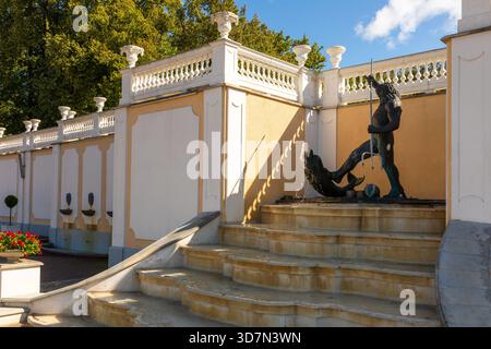Tallinn, Estonie – 02 septembre 2021 : une statue de Neptune se dresse sur une fontaine à marches à côté d'un mur de jardin orné dans un parc historique. Banque D'Images