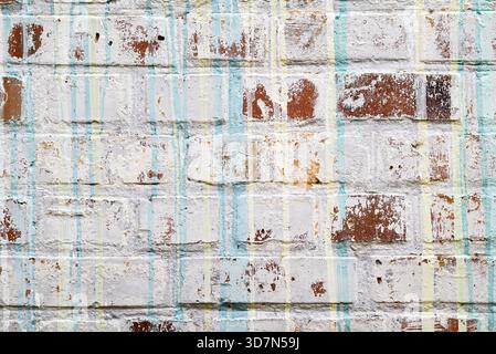 Fond de mur de briques blanches grungy avec peinture pelable et gouttes verticales de peinture bleue et jaune. Banque D'Images