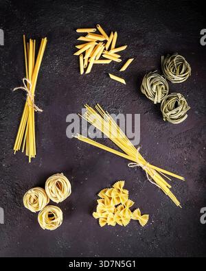 Différents types de pâtes non cuites disposées sur fond d'ardoise rustique Banque D'Images
