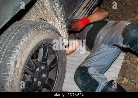 Un mécanicien automobile, allongé sous le fond d'une voiture, effectue l'entretien de la suspension de la voiture sans utiliser de lève-personnes. Banque D'Images