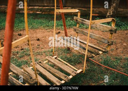 Gros plan détaillé d'une ancienne balançoire en bois avec des planches usées et des supports métalliques jaunes et rouges délavés. Banque D'Images