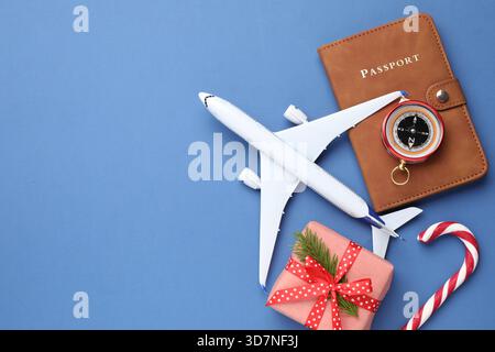Vacances de Noël. Passeport, avion jouet, boussole, boîte cadeau et canne à bonbons sur fond bleu, plat. Espace pour le texte Banque D'Images