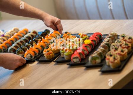 Les mains d'une personne organisent plusieurs grands plateaux gastronomiques de divers rouleaux de sushi, avec des garnitures élaborées comme le saumon, le caviar, et des flocons d'or comestibles Banque D'Images