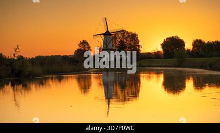 Moulin à vent hollandais traditionnel reflété dans l'eau calme lors d'un lever de soleil doré vibrant Banque D'Images