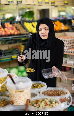 Jeune femme en hijab cueillant des olives au supermarché Banque D'Images
