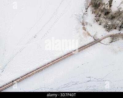 Vue aérienne d'un pont en bois coupant à travers l'étendue gelée, reliant la terre à une petite île sous une couverture de neige, Trakai, Trakai, Lituanie Banque D'Images
