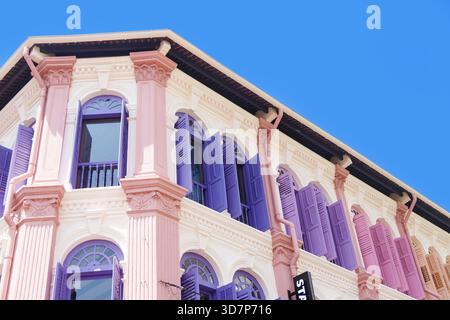 Bâtiment coloré de style colonial avec fenêtres cintrées et volets pastel en rose, violet et blanc sous un ciel clair et vibrant singapour Banque D'Images