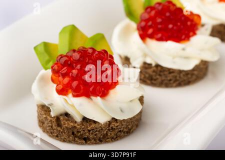 Ces canapés se composent d'une base de pain noir, garnie de tartinade crémeuse et de caviar rouge vif, garni d'avocat Banque D'Images