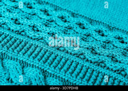Gros plan de tissu de laine tricotée turquoise avec des lignes tressées visibles, des points épais entrelacés et du fil texturé doux formant un textile chaud et confortable Banque D'Images