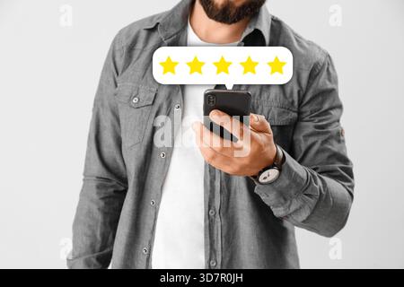 Homme avec téléphone portable donnant des commentaires sur fond clair, gros plan Banque D'Images