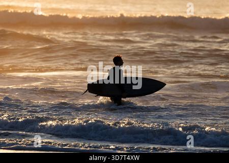 Surfeur marchant sur Ocean Beach au coucher du soleil à San Francisco Banque D'Images