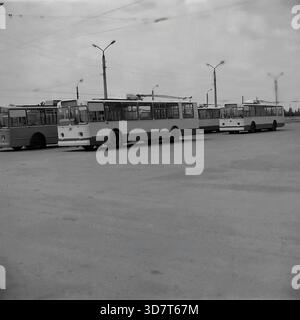 Slavyansk, Ukraine, URSS - 1983 : une flotte de trolleybus soviétiques ZiU-9 est garée en diagonale dans le terrain extérieur du dépôt de l'administration des trolleybus de la ville. Les véhicules électriques s'alignent sur la vaste surface asphaltée sous le réseau complexe de fils de contact aérien. De grands lampadaires en béton se tiennent en arrière-plan. Cette photo d'archives en noir et blanc capture l'échelle du système de transport public, de la logistique de la flotte et de l'atmosphère industrielle de la paisible ville du Donbass. Banque D'Images