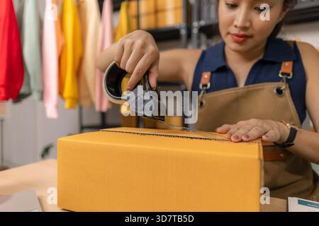 Jeune femme entrepreneure scellant soigneusement le paquet avec du ruban adhésif, préparant les commandes de marchandises, gérant l'expédition et la livraison pour son succès en ligne Banque D'Images