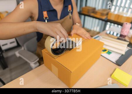 Jeune femme entrepreneure scellant soigneusement le paquet avec du ruban adhésif, préparant les commandes de marchandises, gérant l'expédition et la livraison pour son succès en ligne Banque D'Images