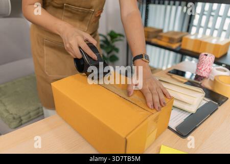 Jeune femme entrepreneure scellant soigneusement le paquet avec du ruban adhésif, préparant les commandes de marchandises, gérant l'expédition et la livraison pour son succès en ligne Banque D'Images