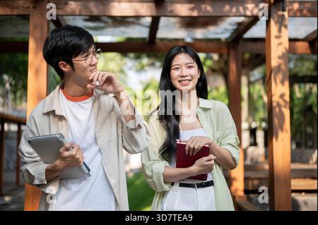 Des amis asiatiques ou un couple d'homme et de femme rient en marchant ensemble dans un couloir en bois. Travailler ou étudier en plein air, Garden Cafe ou Restaurant Banque D'Images