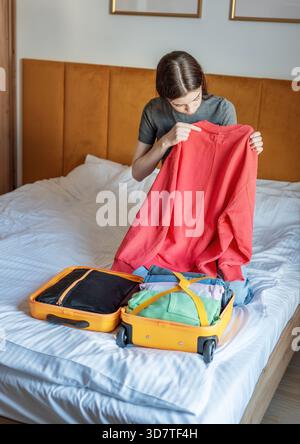 Jeune femme emballant une valise sur le lit, choisissant des vêtements pour un voyage Banque D'Images